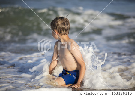 Joyful boy near the sea plays with the waves. Child resting on the beach 103156119