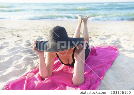 Big beach hat female figure on a background of the sea. Summer vacation on the beach.Woman in a hat sunbathes Big beach hat female figure on a background of the sea. Summer vacation on the beach.Woman in a hat sunbathes 103156190