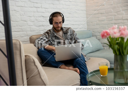 Man gamer playing on laptop on cough, having online network game, using headphones and microphone 103156337