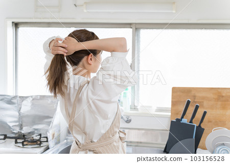 Young woman tying her hair up before starting housework in the kitchen Young woman tying her hair up before starting housework in the kitchen 103156528