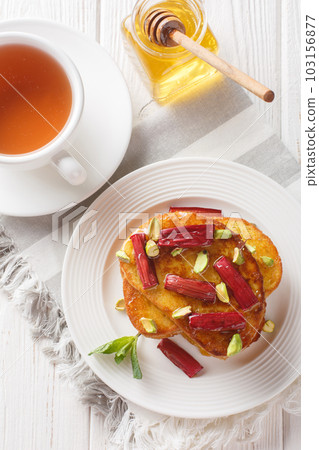 Delicious sweet french toast with baked rhubarb, pistachios, honey served with tea close-up. Vertical top view 103156877