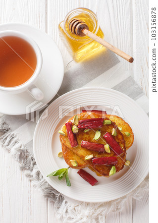 Delicious French toast with baked rhubarb, pistachios and honey close-up on a plate. Vertical top view 103156878