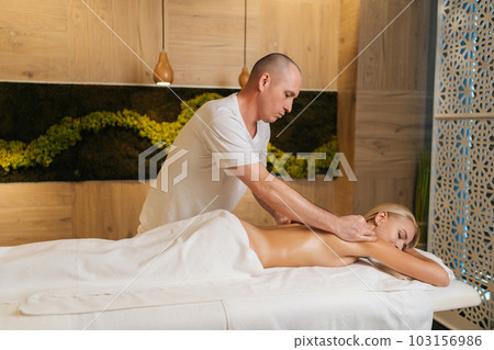 Professional male masseur massages neck and shoulders of young woman in  massage parlor., Stock image