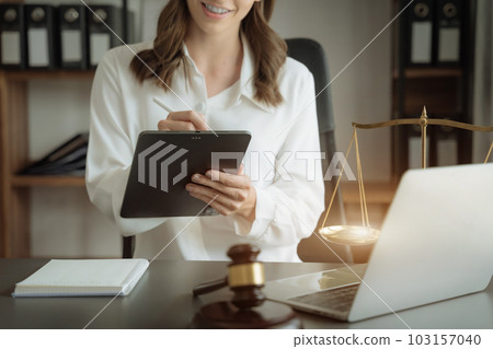 Justice and law concept.Female judge in a courtroom the gavel, working with digital tablet computer on wood table in sun light. 103157040