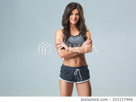 Beautiful smiling young sportswoman in gray top and black shorts standing on gray background Beautiful smiling young sportswoman in gray top and black shorts standing on gray background 103157466