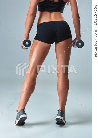 Athletic woman pumping up muscles with dumbbells on gray background 103157556