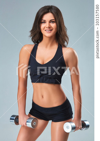 Athletic woman pumping up muscles with dumbbells on gray background 103157580