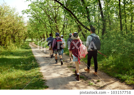 Active, sportive young people, friends going hiking in forest on warm spring day, walking on path, enjoying landscapes. Back view Active, sportive young people, friends going hiking in forest on warm spring day, walking on path, enjoying landscapes. Back view 103157758