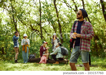 Young man in checkered shirt and sunglasses going hiking with friends. Group of young people walking in forest 103157760