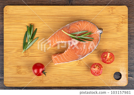 Top view of raw salmon or trout steak, with rosemary and cherry tomatoes on a cutting board. Top view of raw salmon or trout steak, with rosemary and cherry tomatoes on a cutting board. 103157981