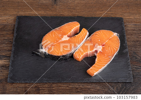 Raw salmon steaks on stone serving board over wooden background. Raw salmon steaks on stone serving board over wooden background. 103157983