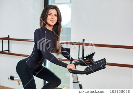 Muscular young woman working out on the exercise bike at the gym, intense cardio workout. 103158058