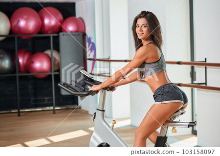 Muscular young woman working out on the exercise bike at the gym, intense cardio workout. Muscular young woman working out on the exercise bike at the gym, intense cardio workout. 103158097