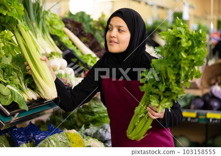 Muslim female seller in apron takes celery leaf from window 103158555