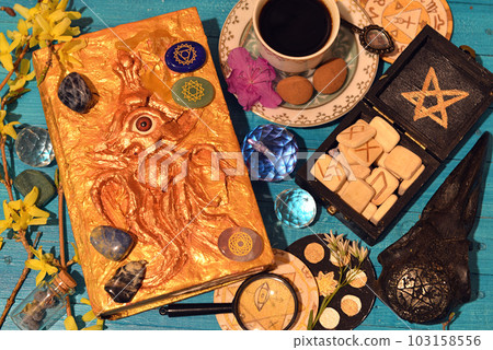 Magic book of spells, runes and cup on witch altar table. Occult, esoteric and divination still life. Mystic background with vintage objects 103158556