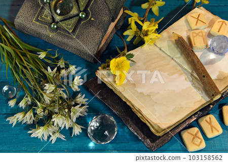 Book of spells, open diary and runes with flowers on ritual altar table. Occult, esoteric and divination still life. Mystic background with vintage objects 103158562
