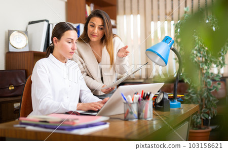 Woman assistant standing with documents near boss in office 103158621