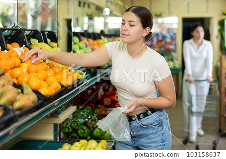 Happy smiling woman making purchases in supermarket, choosing fresh tangerines Happy smiling woman making purchases in supermarket, choosing fresh tangerines 103158637