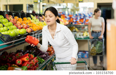 Young woman buys bell pepper at grocery store 103158700