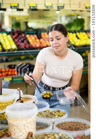 Young woman puts handful of olives in disposable container with ladle 103158806