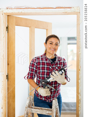 Woman herself installs a wooden door in the room - fills gaps with mounting foam Woman herself installs a wooden door in the room - fills gaps with mounting foam 103158814