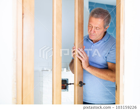 Ordinary elderly man checks the quality of the installed wooden door Ordinary elderly man checks the quality of the installed wooden door 103159226