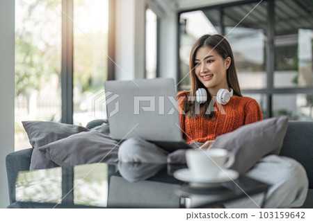 Young business freelance Asian woman working on laptop checking social media while lying on the sofa when relax in living room at home 103159642