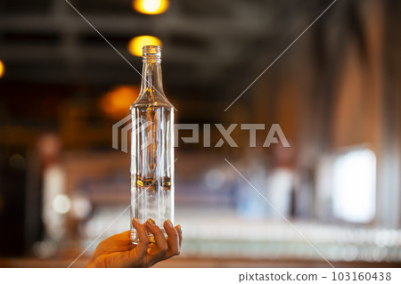 Hand with a bottle on the background of a blurred glass manufacturing workshop. Hand with a bottle on the background of a blurred glass manufacturing workshop. 103160438