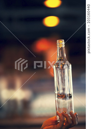 A vertical hand with a bottle on the background of a blurred glass manufacturing workshop. A vertical hand with a bottle on the background of a blurred glass manufacturing workshop. 103160440