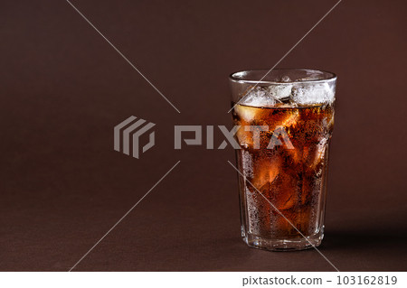 A glass of cola drink with ice cubes. Fresh cold sweet cola drink with ice one brown background with copy space. A glass of cola drink with ice cubes. Fresh cold sweet cola drink with ice one brown background with copy space. 103162819