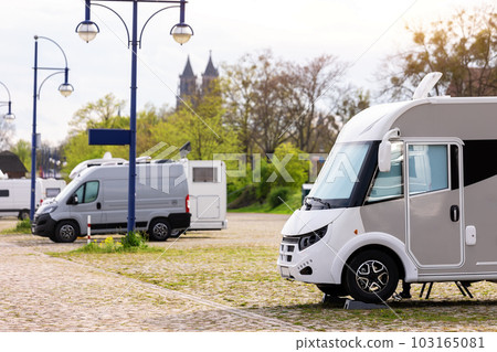 Many white modern campervan recreational motor home vehicles parked in row at camper park site Magdeburg city against Elbe river bridge. Motorhome campground stataion travel destination. RV lifestyle Many white modern campervan recreational motor home vehicles parked in row at camper park site Magdeburg city against Elbe river bridge. Motorhome campground stataion travel destination. RV lifestyle 103165081
