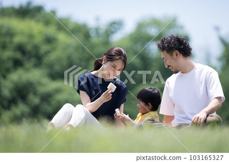 一家人在公園的草坪上放鬆,在休閒床單上吃三明治,還有復印空間 一家人在公園的草坪上放鬆,在休閒床單上吃三明治,還有復印空間 103165327