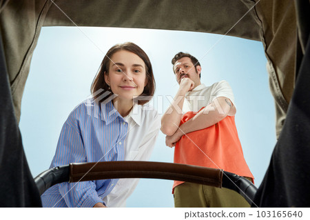 Man and woman, happy parents looking into baby carriage. Mother with happy, delightful face, father with scared funny expression 103165640