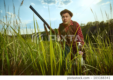 Man hunting and searching prey with his dog English springer spaniel over nature background. Front view. People and animals friendship. Concept of hunting season Man hunting and searching prey with his dog English springer spaniel over nature background. Front view. People and animals friendship. Concept of hunting season 103166341
