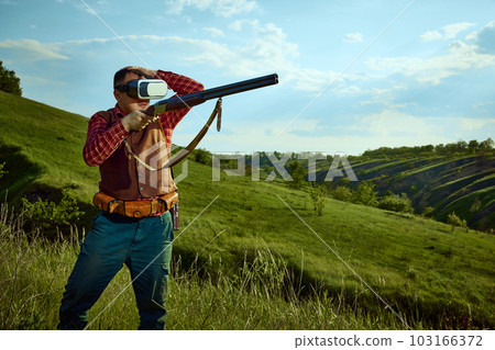 Portrait with adult man wearing VR glasses standing over landscapes background. Online hunting. Concept of virtual reality, video games, hunting season 103166372