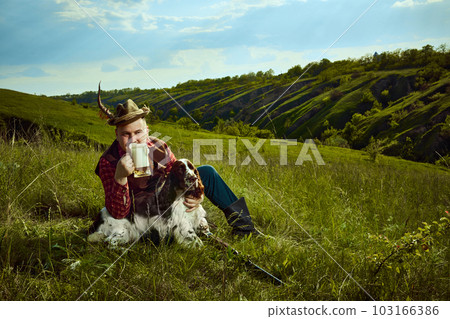Portrait with happy man and his dog English springer spaniel sitting on grass and drinking beer after hunting on beautiful nature landscape background Portrait with happy man and his dog English springer spaniel sitting on grass and drinking beer after hunting on beautiful nature landscape background 103166386