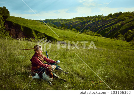 Male hunter in retro suit clothes with hat sitting with dog and waiting for prey animal over picturesque landscapes. Companion dog English springer spaniel Male hunter in retro suit clothes with hat sitting with dog and waiting for prey animal over picturesque landscapes. Companion dog English springer spaniel 103166393