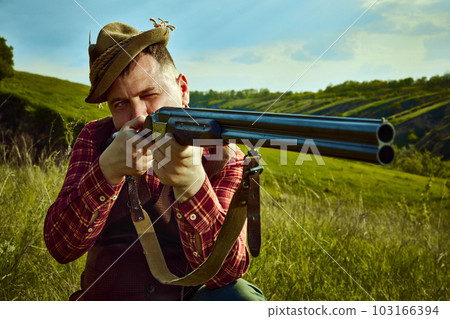 Close up portrait with man, hunter wearing vintage clothes and checked shirt shooting prey with a rifle over marvelous landscapes background 103166394