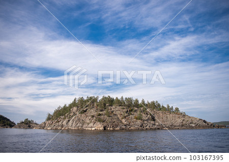Rocky rocks in the lake on the background of a blue sky with clouds Rocky rocks in the lake on the background of a blue sky with clouds 103167395