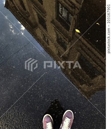 Reflection in a puddle of a building and the legs of a man in sneakers. Reflection in a puddle of a building and the legs of a man in sneakers. 103167901
