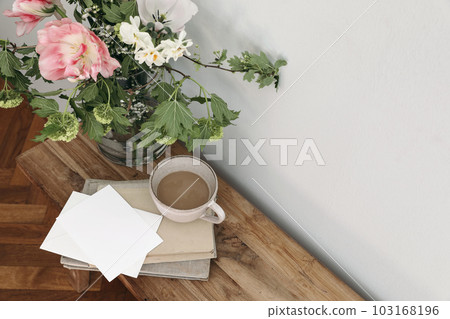 Spring wedding still life. Floral bouquet. Tulips, guelder rose and daffodil flowers. Empty paper card, invitation mockup on vintage bench. Cup of coffee, old books. Blurred wooden floor background. Spring wedding still life. Floral bouquet. Tulips, guelder rose and daffodil flowers. Empty paper card, invitation mockup on vintage bench. Cup of coffee, old books. Blurred wooden floor background. 103168196