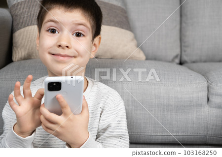 A preschool boy uses a smartphone, plays games on his phone, place for text 103168250