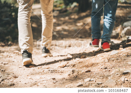 Close-up rear view of tourists heels school boy and his dad walking a stone footpath in spring forest. Child boy and father wearing casual clothes while hiking in summer greenwood forest 103168487