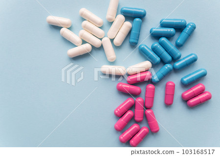 Various colored pills - blue, pink, white, falling out of a plastic bottle, isolated on a blue background. 103168517