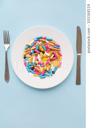Tablets, capsules, vitamins and natural organic food supplements on a white plate on a blue background. Minimal modern pharmacy or healthcare concept. Vertical photo. Tablets, capsules, vitamins and natural organic food supplements on a white plate on a blue background. Minimal modern pharmacy or healthcare concept. Vertical photo. 103168519