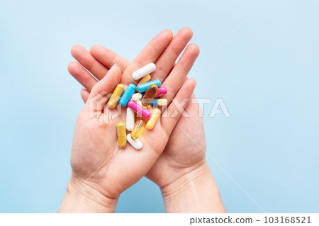 The girl holds a handful of brightly colored vitamins, nutritional supplements, and medicines in her palms. Concept of medicine and health support. The girl holds a handful of brightly colored vitamins, nutritional supplements, and medicines in her palms. Concept of medicine and health support. 103168521