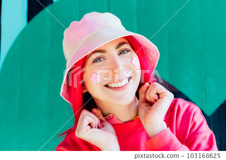 Young woman with pink hair in bright magenta sweatshirt, bucket hat and flower stickers on her cheeks. Anime style. Summer spring urban street fashion. Vanilla Girl. Kawaii vibes. Candy colors design. 103168625