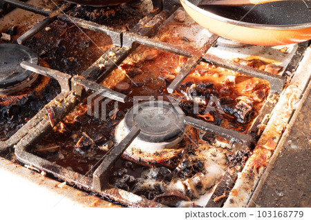 Dirty gas stove surface. Medium gas burner and cast iron grate of a gas oven surrounded by old leftovers of food and drinks. Top area surface and burner heads needs cleaning from burnt-on grease 103168779