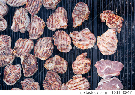 closeup of pork slices being grilled on black iron barbeque grate outdoors closeup of pork slices being grilled on black iron barbeque grate outdoors 103168847