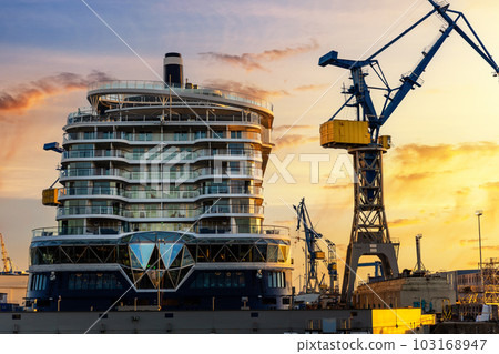 Scenic back view large modern luxury cruise ship liner under construction building cranes at dry dock shipyard in Hamburg port dramatic sunset sky background. Big vessel manufactoring site industry 103168947